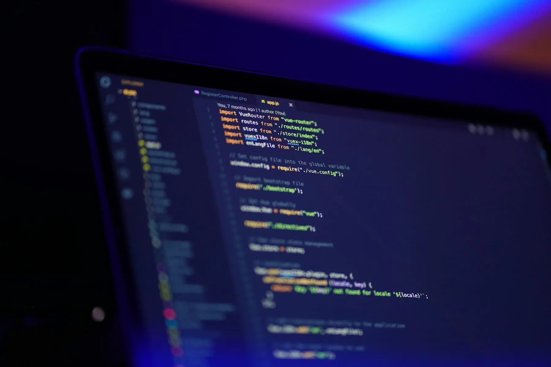 A laptop screen showing source code in a code editor, in a dark room lit in blue. Nobody is in the picture.